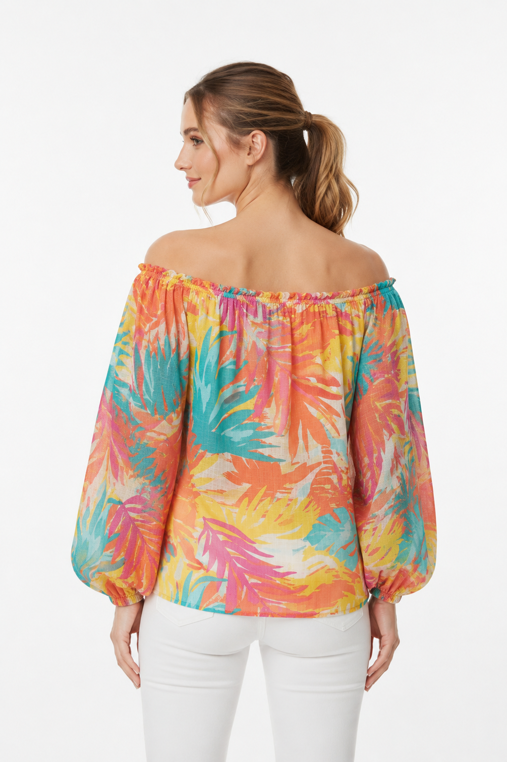 Achterkant van een off-shoulder blouse met tropisch bladprint in oranje, roze, turquoise en geel, met pofmouwen en elastische manchetten, gecombineerd met een witte broek, witte achtergrond.