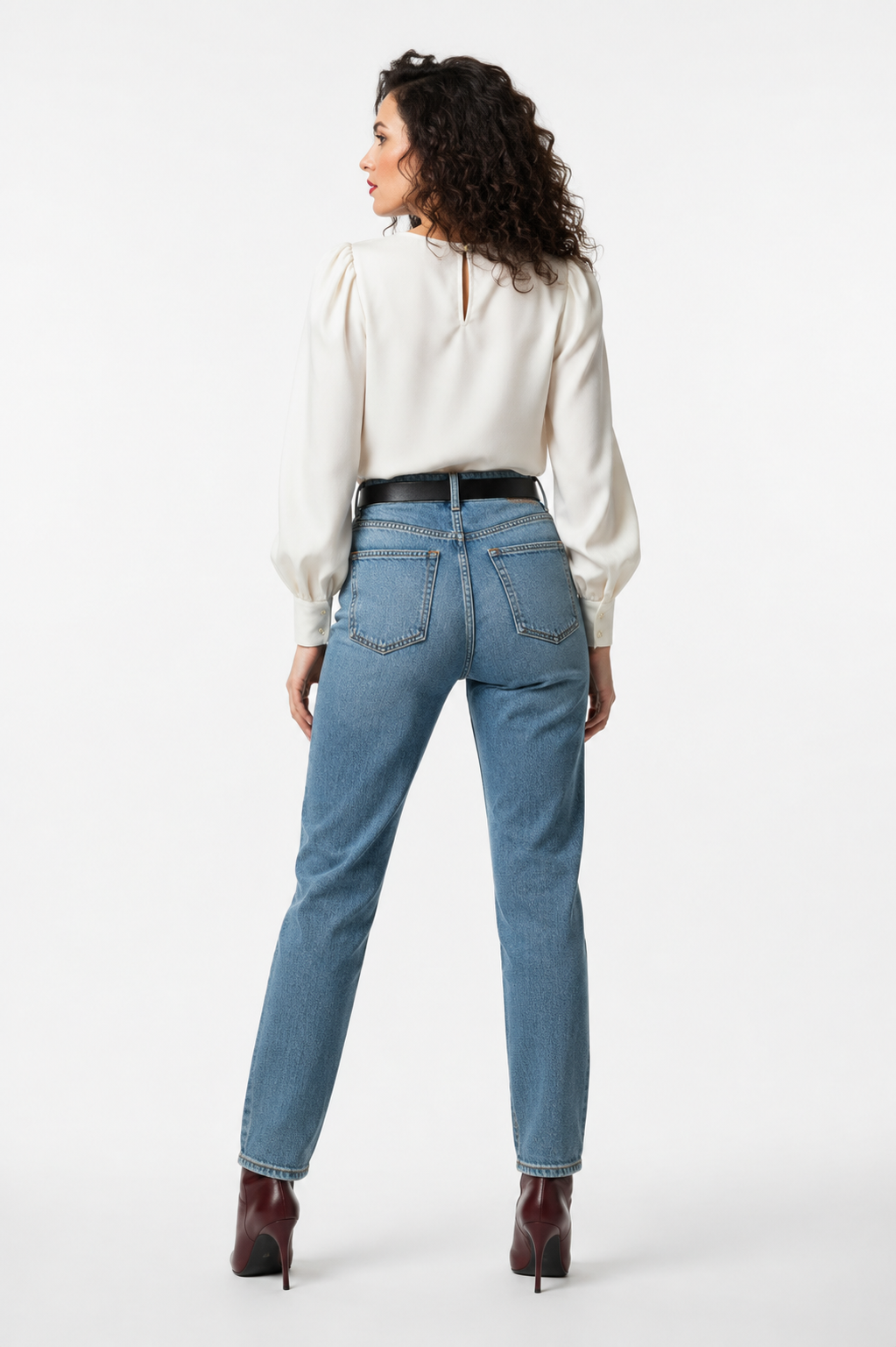 Achterkant van lichtblauwe high-waist straight-fit jeans met twee achterzakken en zwarte riem, gecombineerd met een crèmekleurige satijnen blouse met pofmouwen en bordeauxrode laarzen, witte achtergrond.