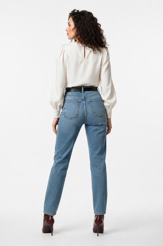 Achterkant van lichtblauwe high-waist straight-fit jeans met twee achterzakken en zwarte riem, gecombineerd met een crèmekleurige satijnen blouse met pofmouwen en bordeauxrode laarzen, witte achtergrond.
