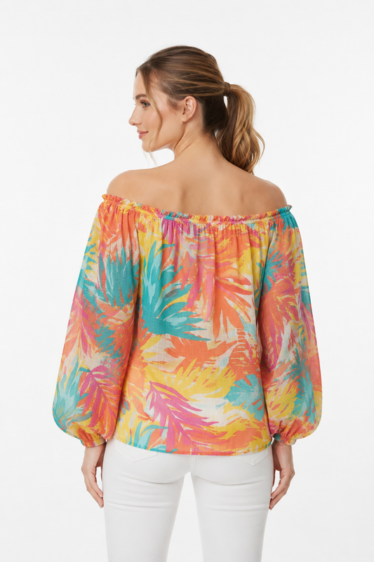 Achterkant van een off-shoulder blouse met tropisch bladprint in oranje, roze, turquoise en geel, met pofmouwen en elastische manchetten, gecombineerd met een witte broek, witte achtergrond.